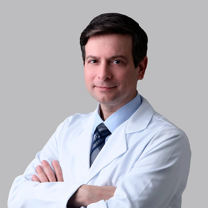 Retrato do Dr. Wener Cella, oftalmologista especialista em retina em São Luís, sorridente, de jaleco branco e braços cruzados sobre fundo cinza