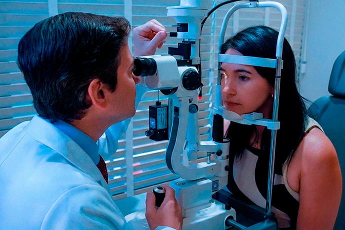 Oftalmologista Dr. Wener Cella examina o olho de uma paciente utilizando um biomicroscópio de lâmpada de fenda branca em um ambiente clínico